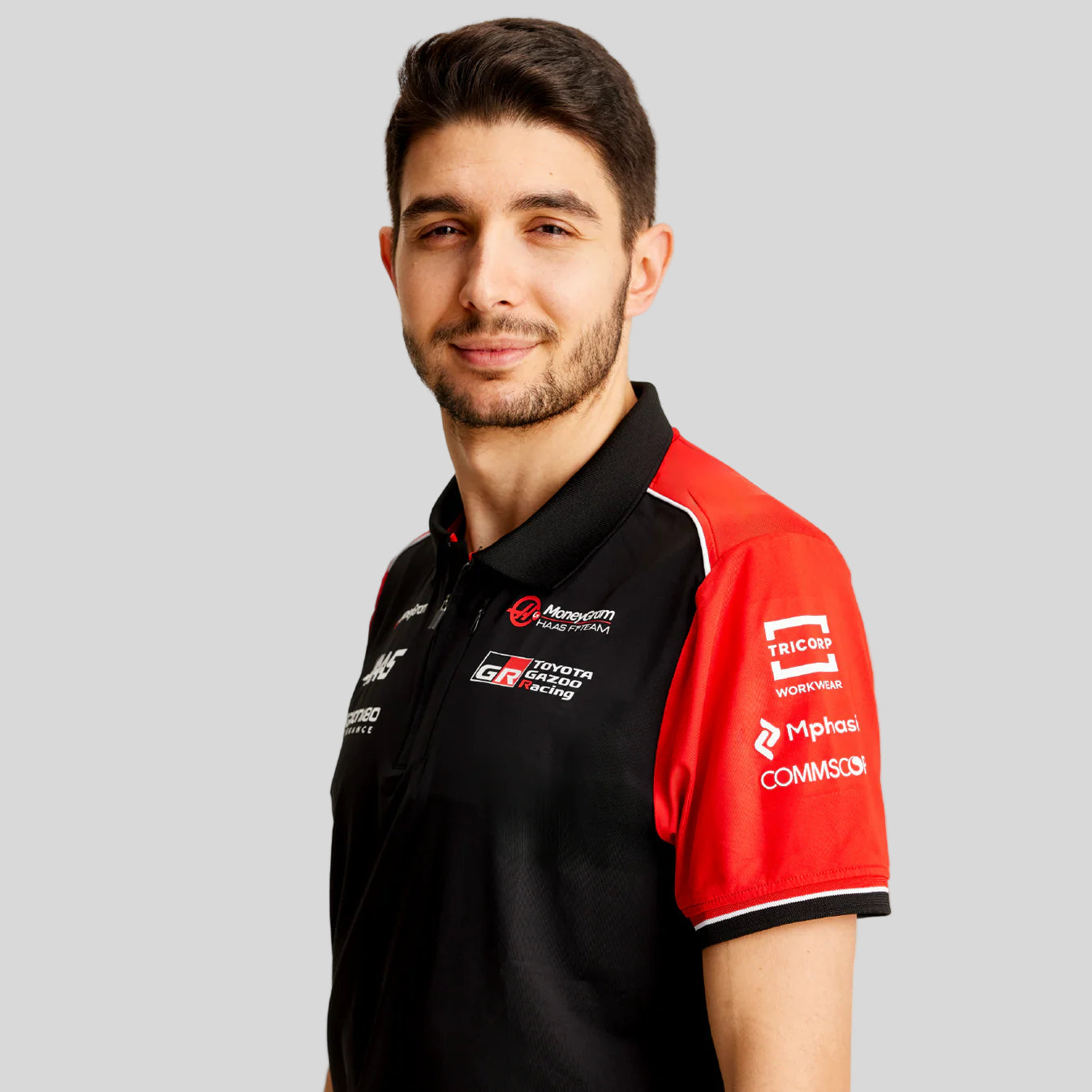 Man wearing a black and red polo shirt with various logos on a light gray background