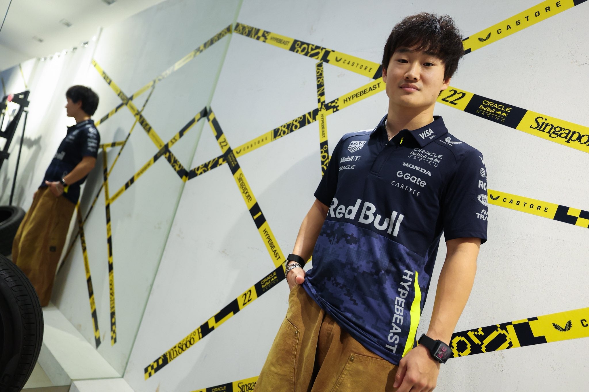 Person wearing a Formula 1 themed shirt with sponsor logos in a room with decorative tape.