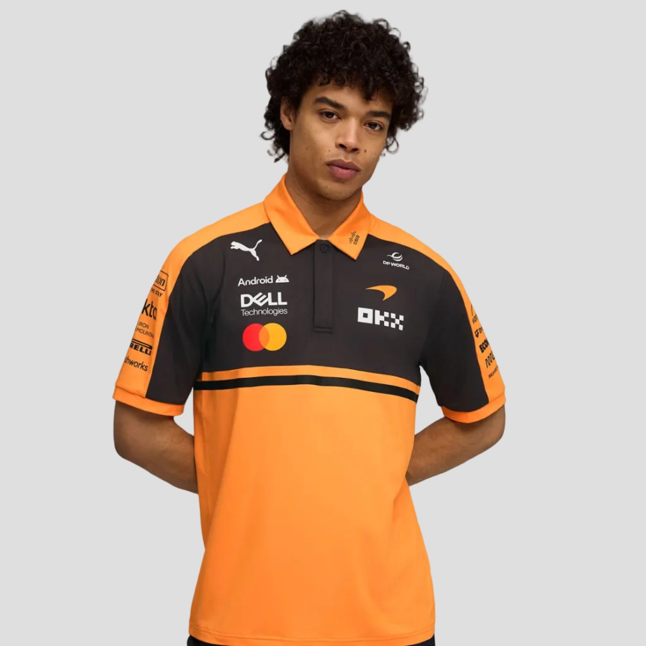 Person wearing an orange and black polo shirt with various logos on a gray background