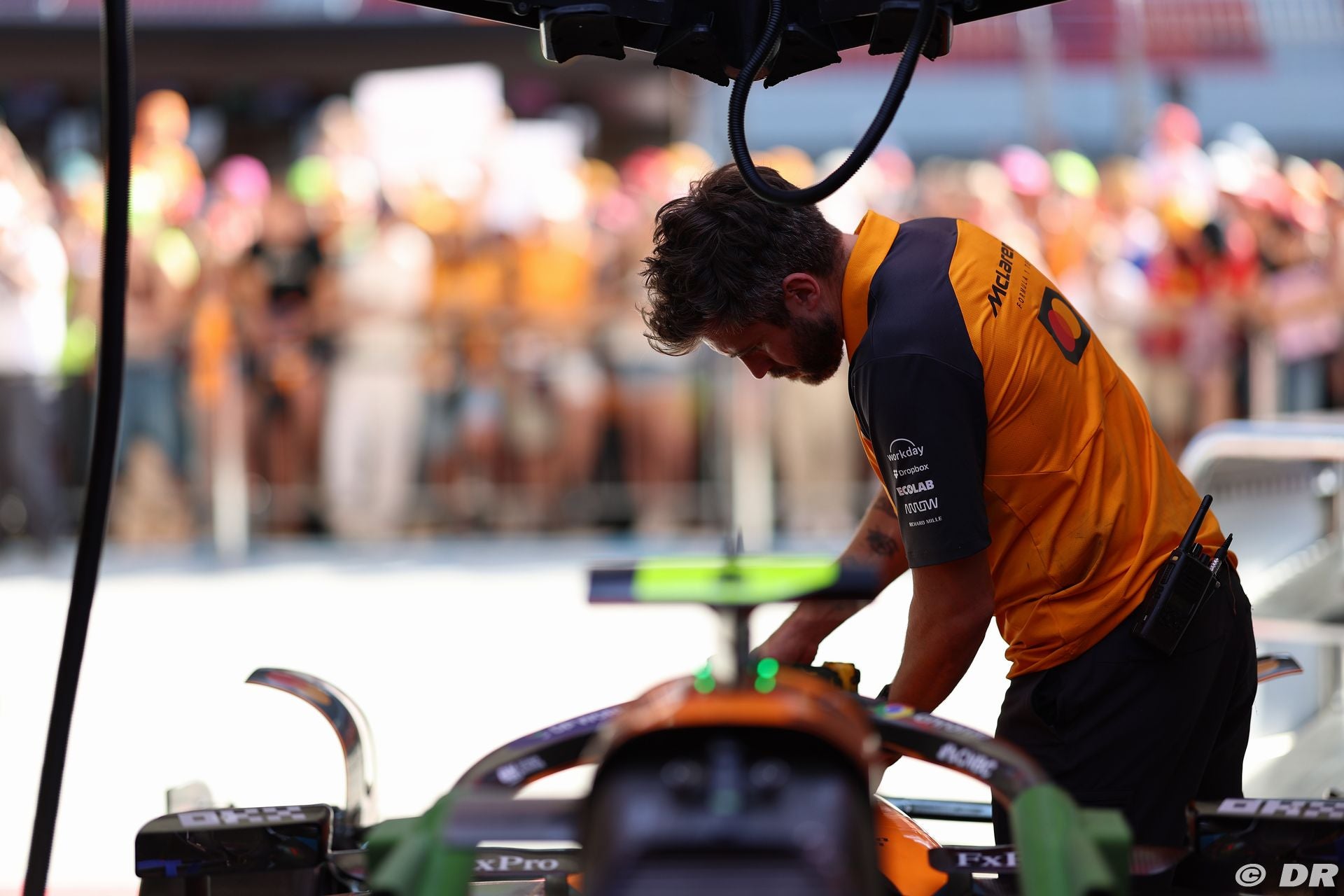 Person working on a Formula 1 car with a blurred crowd in the background